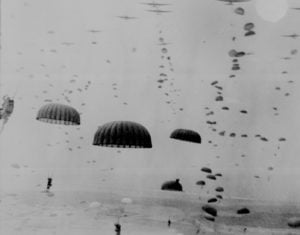 Parachutes open overhead as waves of paratroops land
