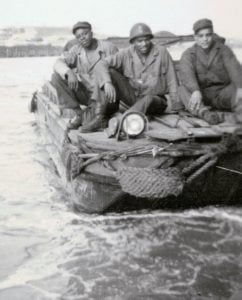 Several African American soldiers sit on top of a WWII DUKW in the water