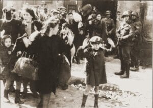 Little Boy raises his hands above his head while Nazi soldiers point weapons at the crowd